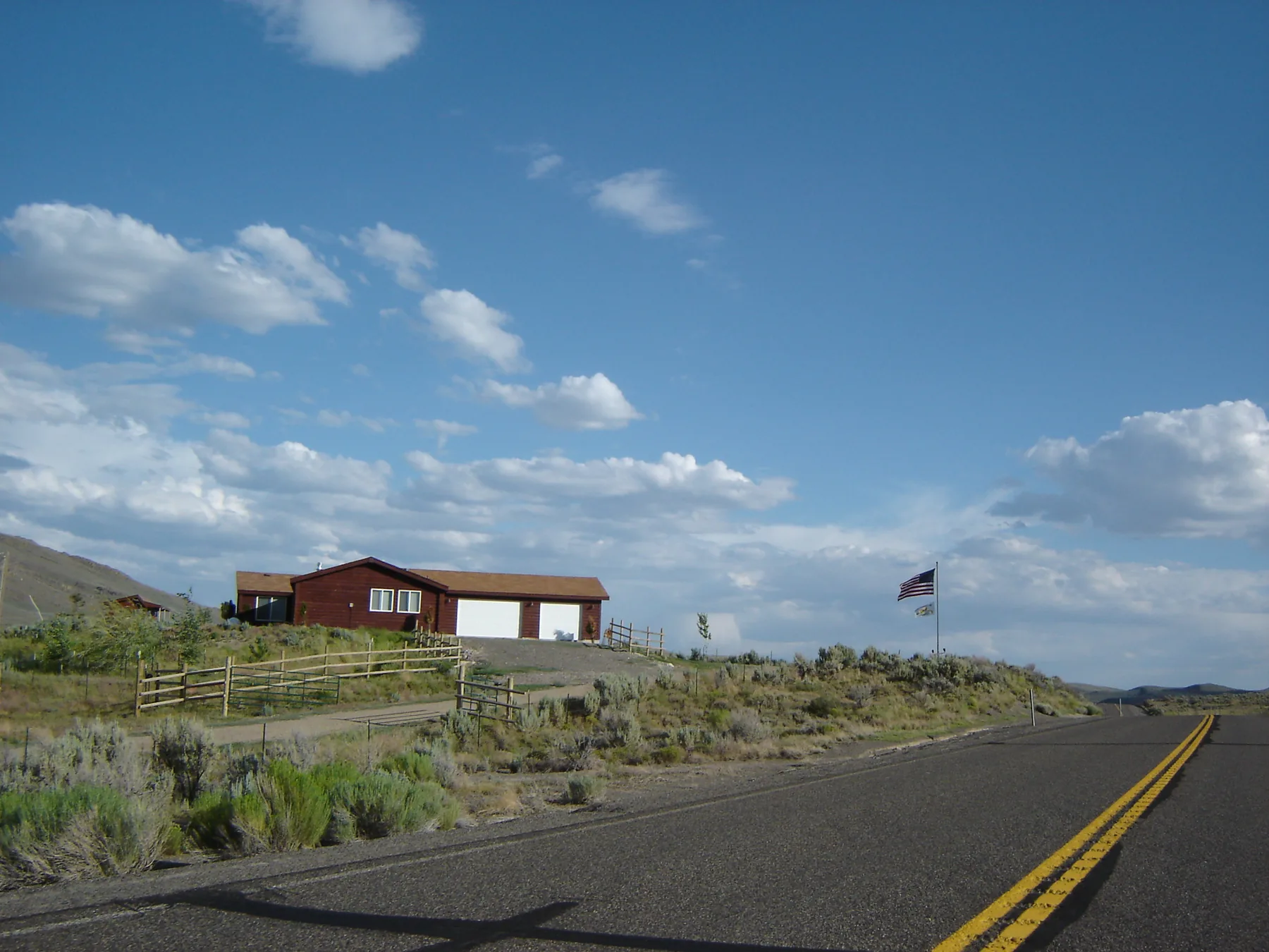 American flag flying above a second flag on a pole beside a rural home