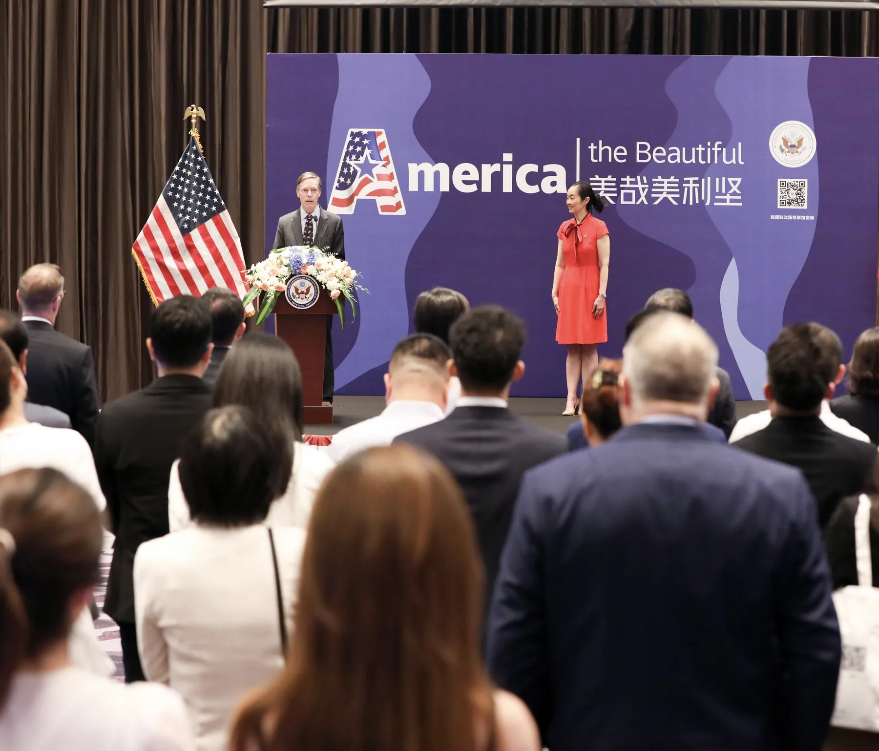 Speaker delivering remarks at a lectern on a stage with a United States flag visible nearby