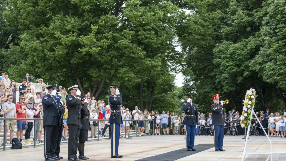 Uniformed honor guard members salute beside a memorial wreath at Arlington National Cemetery